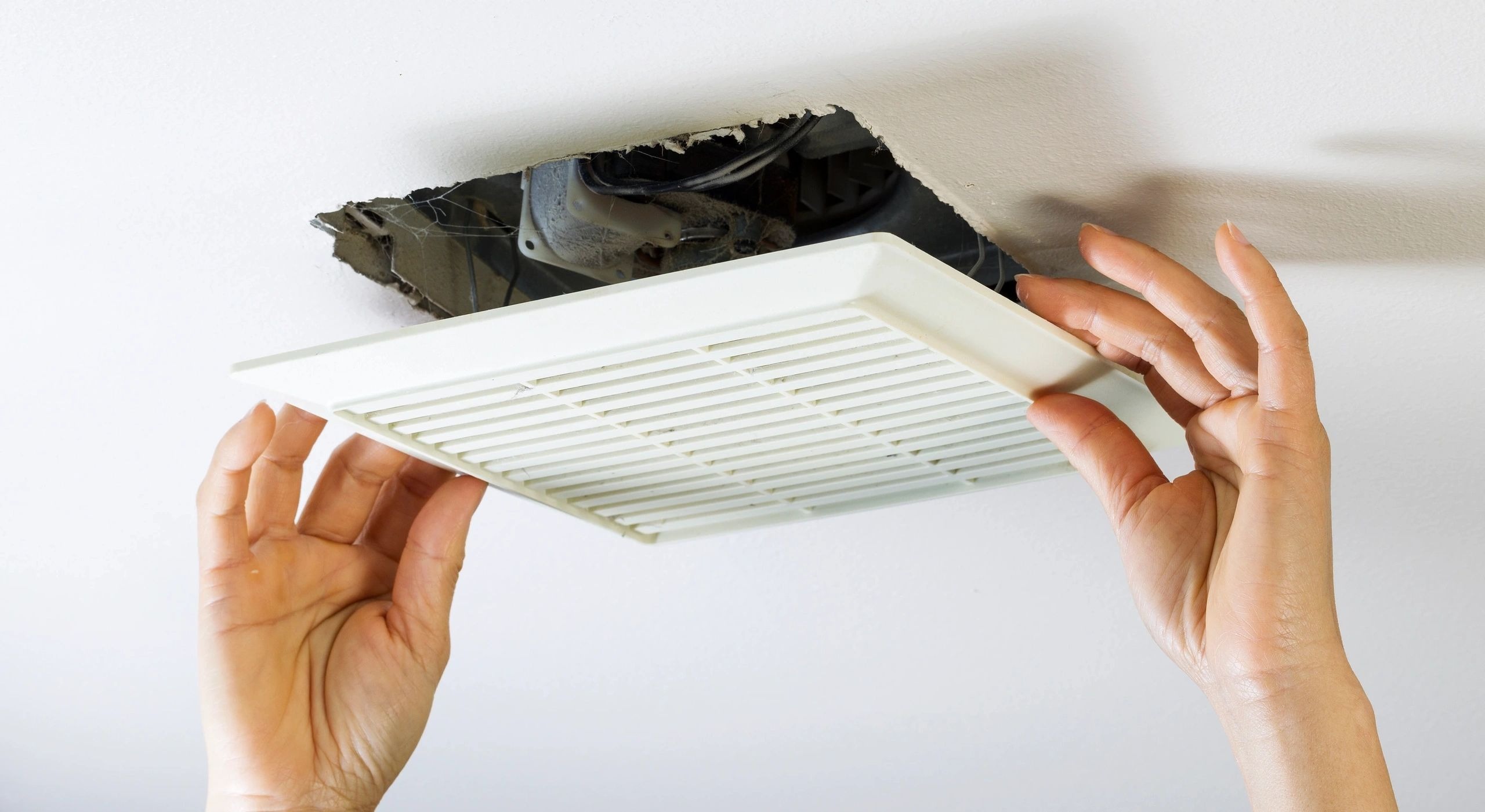 A person is holding the vent cover on an air duct.